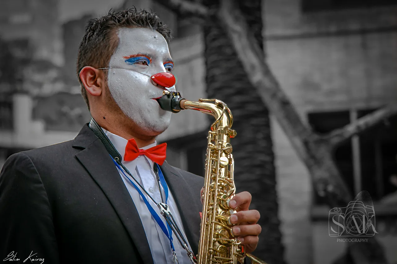 Street musician in clown make-up playing the saxophone